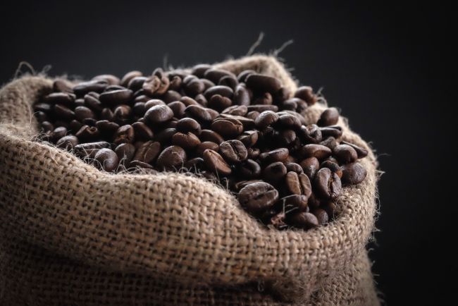 Saco de yute lleno de granos de café tostados sobre un fondo oscuro